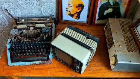 Vintage-typewriter,-old-TV,-and-heater-on-a-wooden-table-with-framed-art-in-the-background