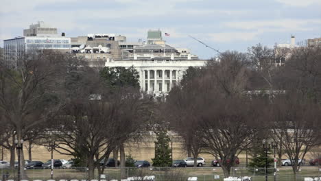 People-walk-past-vehicles-parked-in-front-of-the-lawn-as-a-Stars-and-Stripes-flag-flies-over-the-White-House-official-presidential-residence