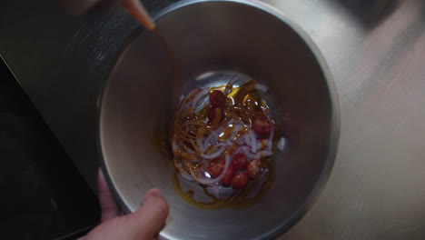 Beautiful-slow-motion-tracking-shot-of-a-chef-pouring-oil-from-a-bottle-into-a-steel-bowl-with-cherry-tomatoes-and-chopped-octopus-pieces-to-cook-fried-octopus-in-a-restaurant-kitchen-in-the-morning