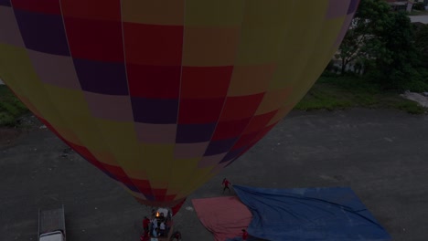 Crew-inflating-a-colorful-hot-air-balloon-on-a-foggy-morning,-preparing-for-flight,-bright-yellow-purple-flame-rises