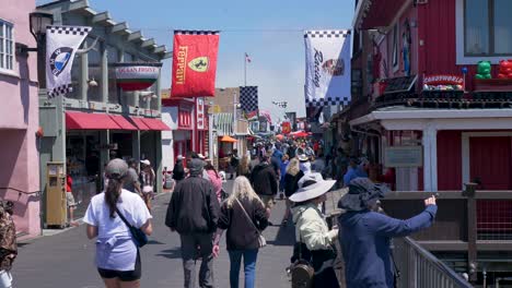 Slow-motion-landscape-shot-of-people-walking-along-Monterey-pier-boardwalk-shopping-with-flags-hanging-on-vacation-holidays-travel-California-coastline-USA-America