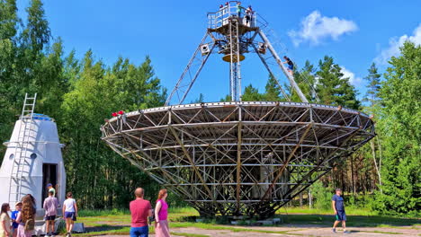 Panoramic-view-of-tourists-visiting-an-RT-32-telescope-in-a-sunny-day-around-green-fields,-skyline-background