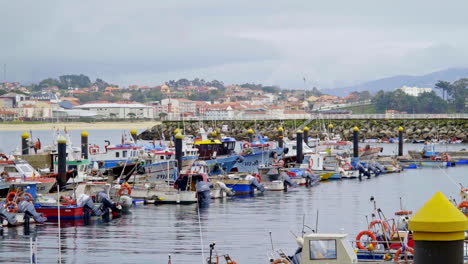 A-serene-coastal-fishing-village-with-colorful-boats-docked-in-a-calm-harbor,-backed-by-a-scenic-townscape-and-mountains