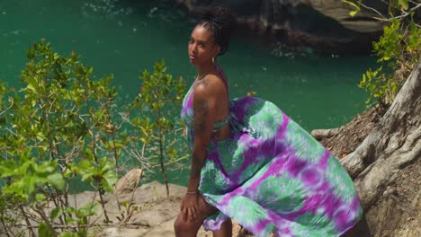 On-the-edge-of-a-cliff,-a-woman-in-a-long,-flowing-dress-takes-in-the-view-of-the-beach-below