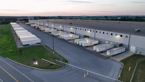 Aerial-approaching-of-industrial-truck-trailers-at-large-warehouse-during-sunrise