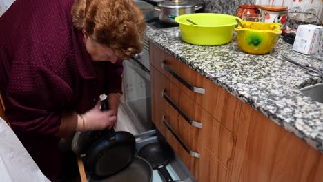 Mujer-Caucásica-Mayor-Inclinándose-Hacia-Adelante-Y-Buscando-Una-Sartén-En-El-Cajón-De-La-Cocina