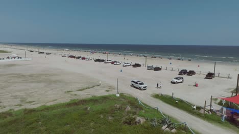 Vista-Aérea-En-4K-Del-Letrero-De-Entrada-A-La-Playa-De-Porretto,-El-área-De-Estacionamiento-Y-Las-Sillas-De-Playa-Y-Sombrillas-En-La-Isla-De-Galveston,-Galveston,-Texas