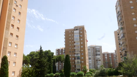 Tall-residential-European-buildings-with-balconies-in-Spain-rise-against-a-clear-sky,-surrounded-by-lush-greenery-and-trees