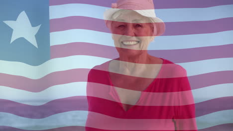 Mujer-Mayor-Sonriente-En-La-Playa-Sobre-Una-Animación-De-Bandera-Estadounidense-Ondeando