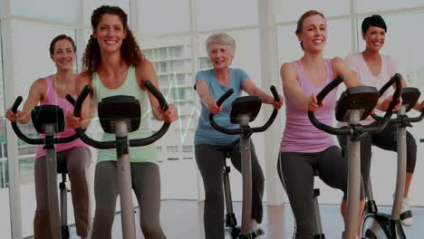 Grupo-De-Mujeres-Haciendo-Ejercicio-En-Bicicletas-Estáticas-Con-Animación-De-Frecuencia-Cardíaca-Sobre-Ellas