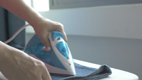 Women-hands-ironing-clothes-with-iron-on-ironing-board