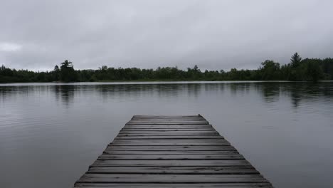 Handheld-POV-from-Narrow-Wooden-Dock-over-Lake-on-Cloudy-Rainy-Dark-Day