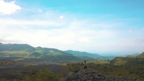 Drone-aerial-flying-over-a-man-spinning-a-staff,-in-a-volcanic-rocky-landscape-near-Pacaya-volcano-in-Guatemala,-Central-america