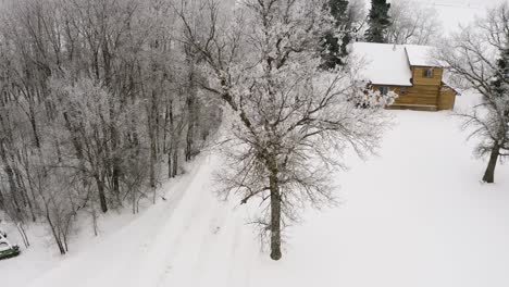 Luftabstieg-Auf-Eine-Ruhige-Und-Warme-Winterblockhütte-Während-Eines-Weichen-Schneefalls-Mit-Brennholz,-Das-Auf-Der-Vorderen-Veranda-Sitzt