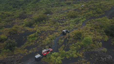 Drone-aerial-flying-towards-cars-driving-off-road-over-volcanic-sand-in-a-forest,-Pacaya-Volcano,-Guatemala
