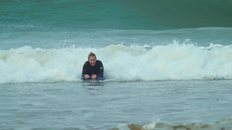 Woman-rides-wave-on-bodyboard-at-beach,-slow-motion