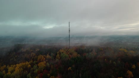 Communication-Tower-Surrounded-By-Colorful-Autumnal-Trees-And-Mist-In-Quebec,-Canada-On-A-Cloudy-Day---aerial-drone,-wide-shot