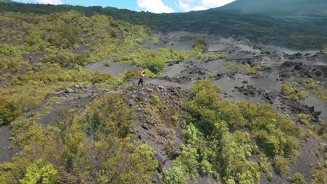 Drone-aerial-rotating-shot-of-a-man-spinning-a-staff,-landscape-with-volcanic-sand-near-Pacaya-volcano-in-Guatemala