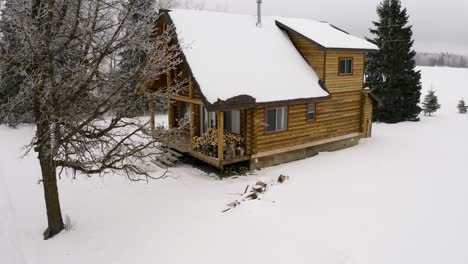 Close-up-slow-aerial-dolly-left-around-a-cozy-warm-log-cabin-in-a-winter-setting-during-a-light-snowfall