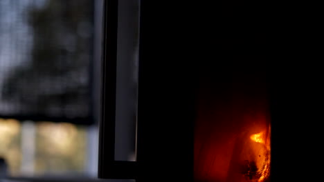 Fire-seen-through-window-in-fireplace-stove,-cozy-hygge-concept,slow-motion