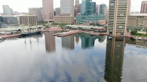 Aerial-tilt-up-reveals-reflection-of-tall-building-in-water-at-Baltimore-Maryland-Inner-Harbor,-top-of-world-aerial-drone-view