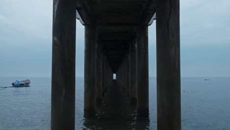 Boat-floating-on-ocean-at-overcast-day-with-under-pier-in-foreground