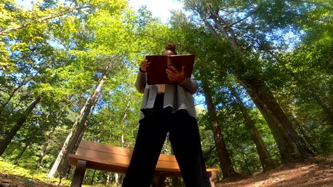Low-angle-shot-of-Black-woman-standing-in-woods-reading-bible