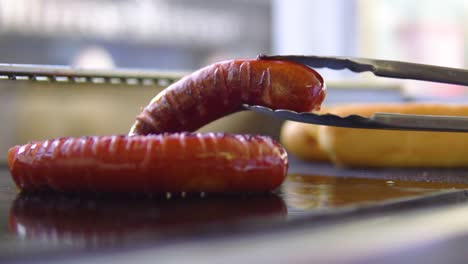 Turning-sausage-around-on-outdoor-grill-at-high-street-in-slowmotion