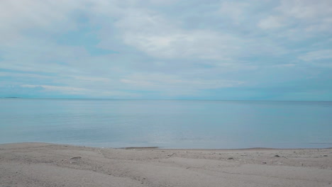 POV-driving-shot-along-sand-beach,-endless-blue-ocean-and-cloudy-sky