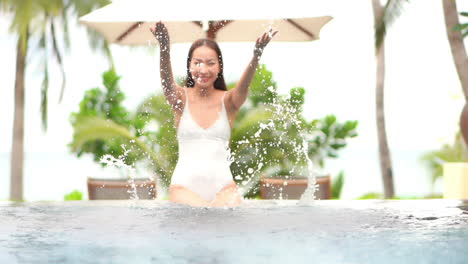 Während-Sie-Am-Rand-Eines-Privaten-Resortpools-Sitzt,-Spritzt-Eine-Hübsche-Frau-In-Einem-Einteiligen-Badeanzug-Wasser-In-Die-Luft