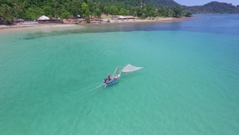Aerial-dolly-shot-of-a-traditional-shrimp-fisherman-on-small-wooden-boat-in-Thailand-with-beach-and-resorts-in-the-background