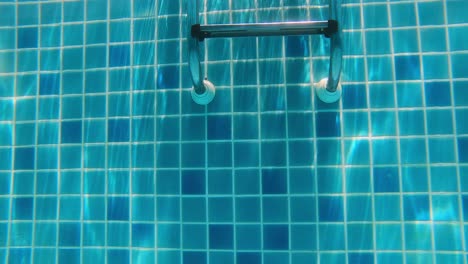 Underwater-footage-of-walking-along-the-bottom-of-a-swimming-pool-towards-a-ladder