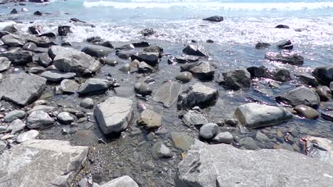 Eine-Nahaufnahme-Eines-Seeufers-Mit-Sichtbarkeit-Von-Steinen-Und-Kieseln-Unter-Wasser-Und-Ruhigem-Wellenläppen