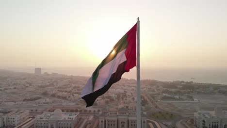 Bandera-De-Los-Emiratos-árabes-Unidos-Ondeando-En-El-Viento,-El-Cielo-Y-El-Fondo-Del-Sol-El-Símbolo-Nacional-De-Los-Emiratos-árabes-Unidos-Sobre-La-Isla-De-La-Bandera-De-Sharjah,-Emiratos-árabes-Unidos