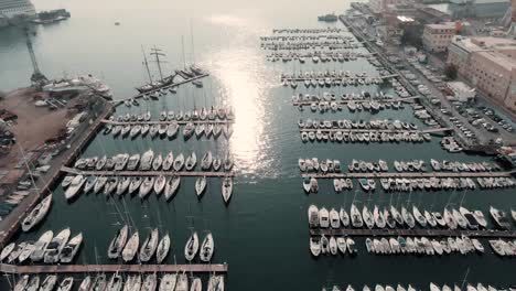 Flying-Over-The-Sailboats-Moored-At-The-Quay-On-A-Sunny-Day-In-Genoa-In-Liguria,-Italy