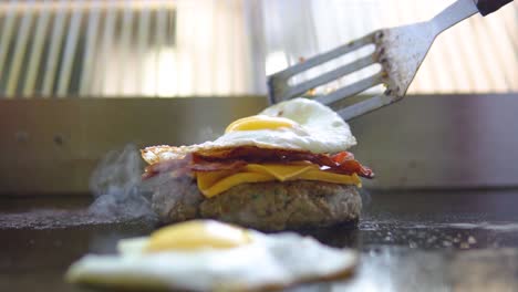 Placing-freshly-cooked-bacon-and-egg-on-a-cheeseburger-which-is-still-being-grilled-in-fast-food-restaurant