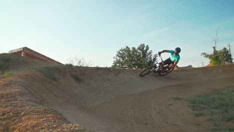 Man-on-mountain-bike-whips-around-on-a-dirt-turn-in-a-bike-park,-before-he-whips-in-front-of-the-camera
