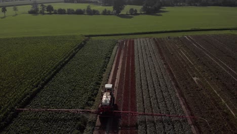 Aerial-ascend-and-fly-over-a-tractor-dragging-wide-spraying-arms-and-stock-of-liquid-in-Dutch-farmland