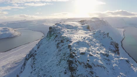 Drone-flying-over-top-of-Beautiful-snowy-white-mountains-to-the-sun-of-the-Westfjords-in-Iceland-between-sea-shore--aerial