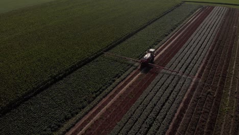 Aerial-view-of-a-tractor-dragging-wide-spraying-arms-and-stock-of-liquid-in-farmland-landscape