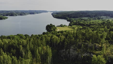 Aerial-shot-of-forested-hills-and-large-lake-in-Sweden,-forward-motion