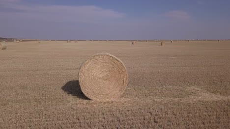 Orbiting-aerial-of-gold-hay-bale-in-fresh-cut-field-with-crisp-horizon