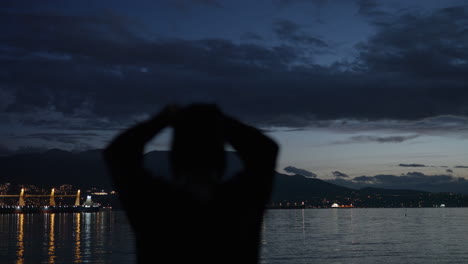 Silhouette-of-woman-looking-at-city-lights-of-Vancouver,-Canada-across-water