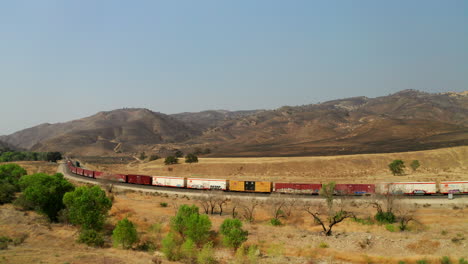 A-freight-train-is-parked-along-tracks-below-hells-left-burnt-by-wildfires---aerial-parallax-view