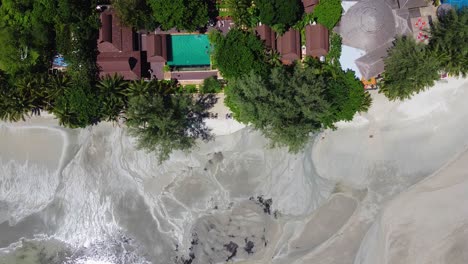 AERIAL:-Static-Drone-shot-of-The-Hotel-with-a-swimming-pool-on-the-Coastline,-low-tide-at-the-Ocean