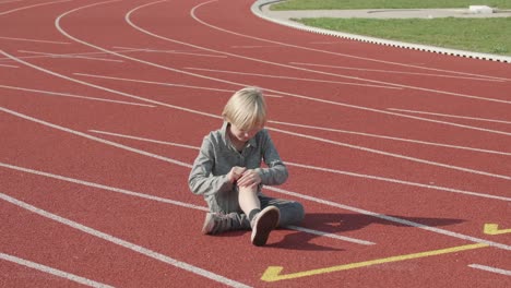 blond-European-boy-sitting-on-a-running-track-with-a-hurt-knee