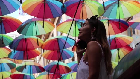 Mädchen,-Das-Farbige-Regenschirme-Aufschaut-Und-Glücklich-Am-Telefon-Spricht