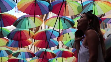 Mädchen,-Das-Am-Telefon-Spricht-Und-Farbige-Regenschirme-In-Ehrfurcht-In-Zeitlupe-Betrachtet