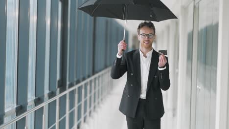 Happy-young-man-standing-in-the-hallway-opens-an-umbrella-and-shows-a-plastic-card