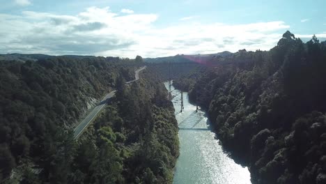 Aerial-view,-flying-over-a-road-and-a-river-towards-an-abandoned-bridge-on-a-sunny-day-in-New-Zealand,-dolly-shot